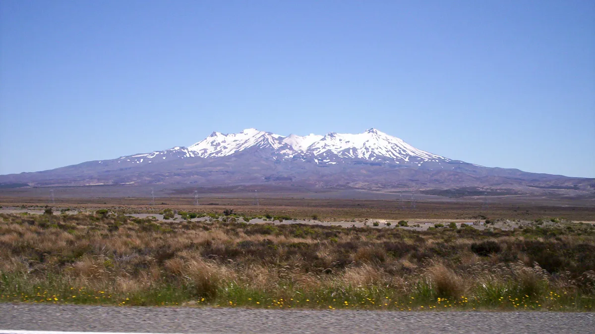 Snow-capped volcanic alpine peak rising above rugged gravel terrain
